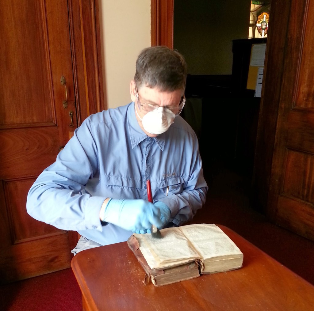 A conservator with mask and gloves carefully dusting the inside of one of the books in the collection.